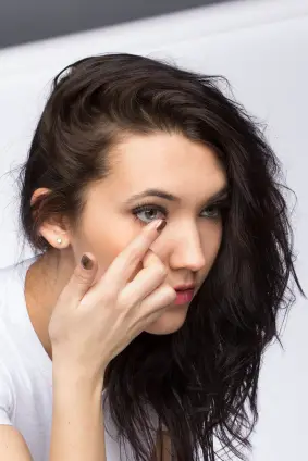 A woman inserts a contact lens into her eye