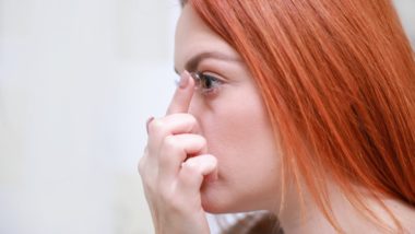 Girl with red hair inserting a contact lens into her eye