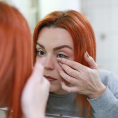 Girl inserting a contact lens in the mirror